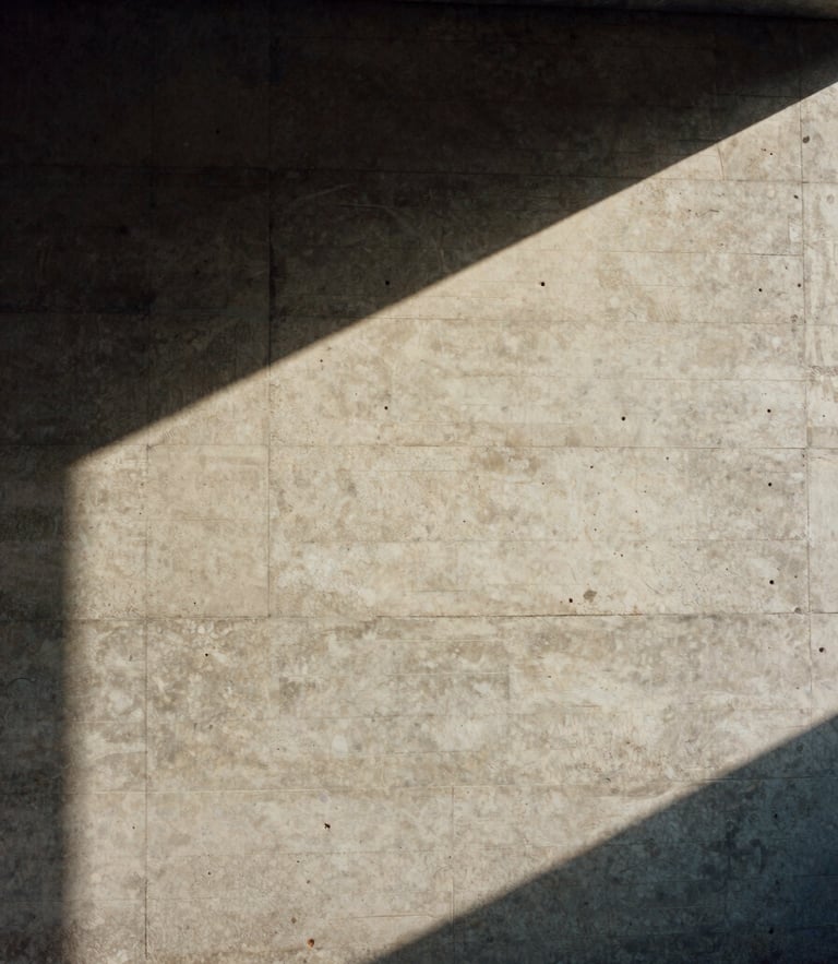 Cinematic film photography of a concrete modernist studio wall with a single ray of sharp sunlight cutting across the raw texture, desaturated earth tones, 35mm grain