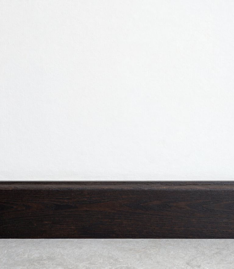 Straight-on architectural shot of a perfectly aligned, hand-wiped dark wood baseboard meeting a crisp linen-white wall, bright natural daylight, clean lines.