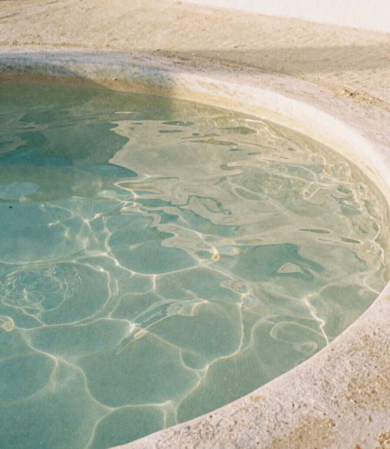 Extreme close-up of warm rippling thermal water in a stone pool, soft morning daylight filtering through, minimalist Mediterranean architecture, 35mm film style.
