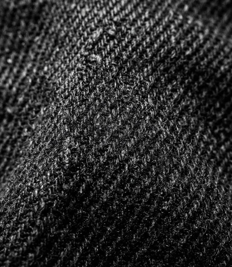 Extreme close-up of heavy black cotton fabric texture, stark studio lighting, high-contrast, sharp shadows, brutalist composition, 35mm film grain
