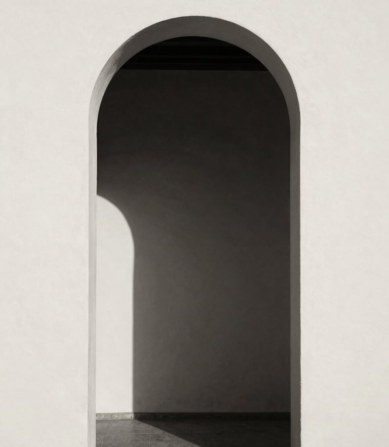 Minimalist architectural archway in Spain, soft natural window light casting deep shadows on a warm cream plaster wall, high contrast black and white photography, sepia undertone, 35mm film grain