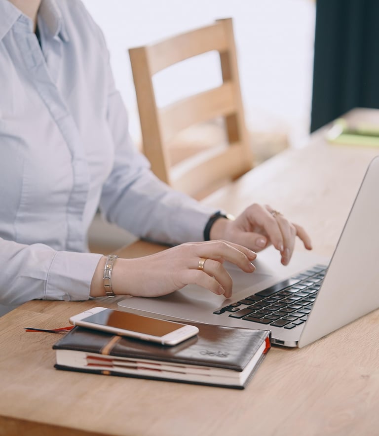 Businesswoman typing on a laptop at a wooden desk with a smartphone and notebook.