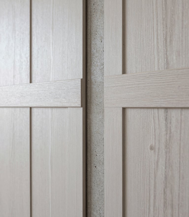 Macro photograph of a premium material junction showing white oak paneling meeting a raw concrete column, soft diffused daylight, sharp focus.