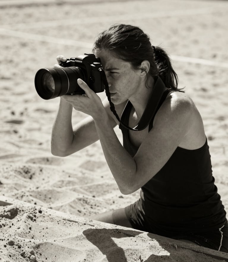 Dramatic black and white portrait of a female photographer holding a professional camera, low angle, sand court background with harsh sunlight and deep shadows, 85mm
