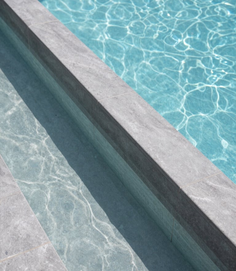 Close-up of a luxury zero-edge pool overflow channel with crystal clear water and precise graphite grey tiling under bright daylight