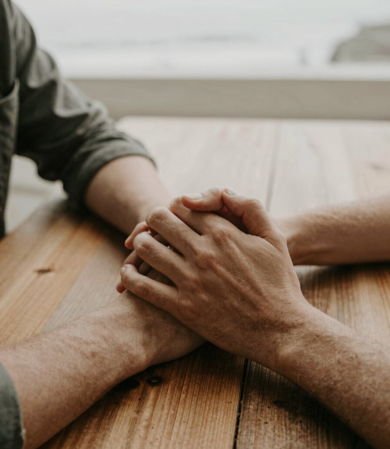 A candid, warm close-up of two people holding hands over a wooden table, soft Pacific Northwest overcast daylight, muted earthy tones, 35mm.