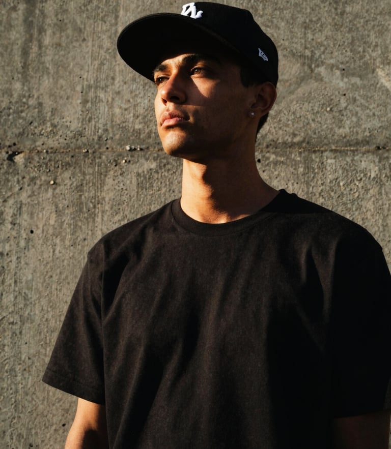 Low-angle portrait of a streetwear model wearing a structured black snapback cap against a raw concrete wall in Karachi, dramatic high-contrast lighting, 35mm film style
