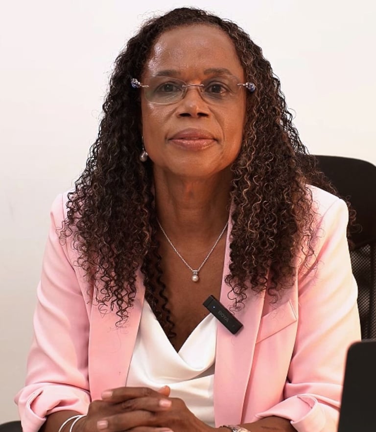 Professional woman with curly hair wearing a pink blazer and glasses in an office setting.