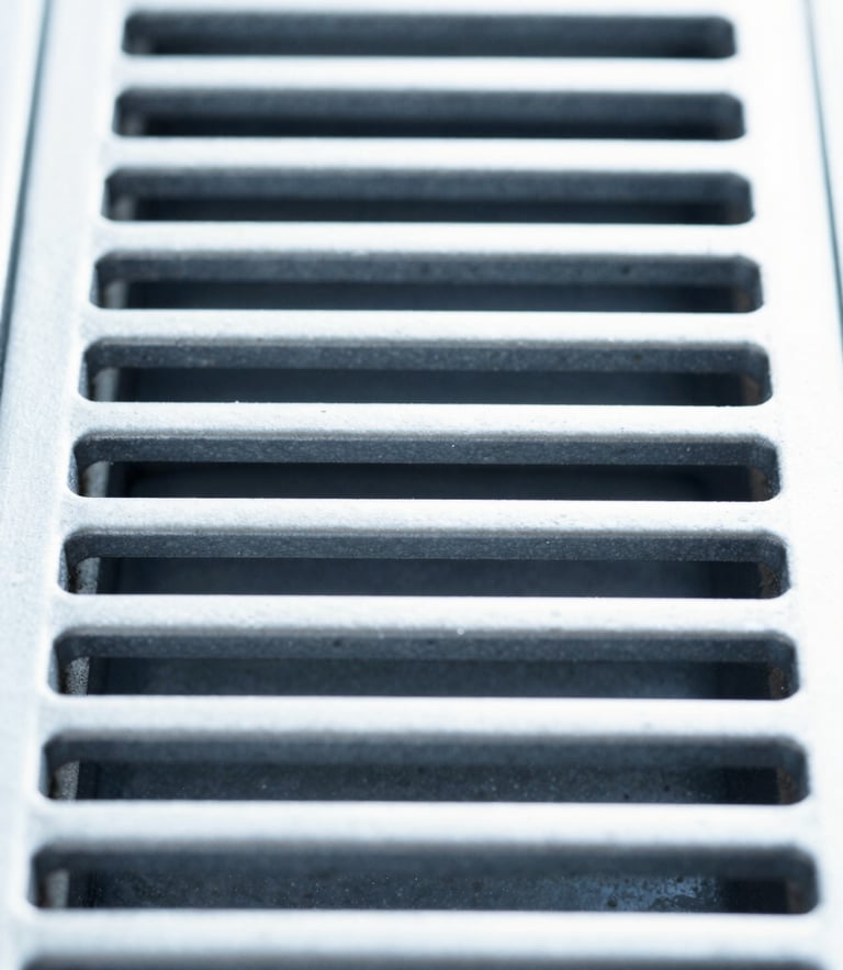Straight-on symmetrical macro shot of a pristine clean metallic ventilation grate, bright high-key daylight, clinical cool blue tones, sharp focus.