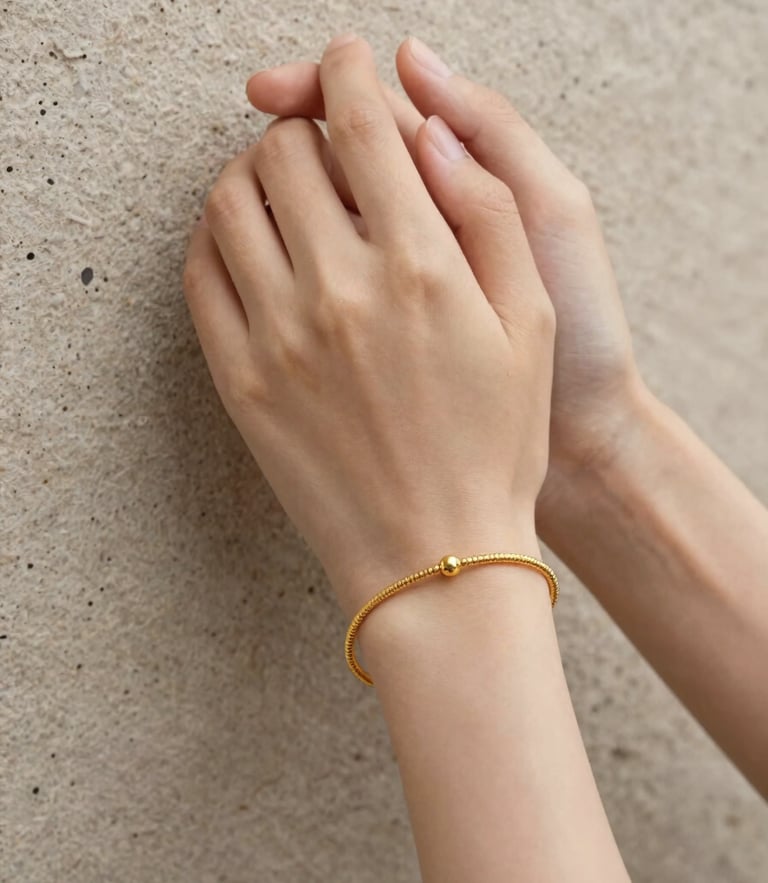 Hands clasping a whisper-thin gold bracelet against a textured stone background, soft diffused lighting, editorial jewelry photography.