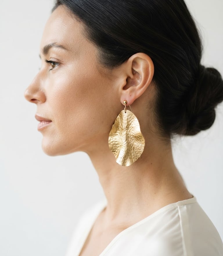Close-up profile of an elegant woman wearing a large gold-textured leather earring, soft natural daylight, minimalist white background, editorial crop