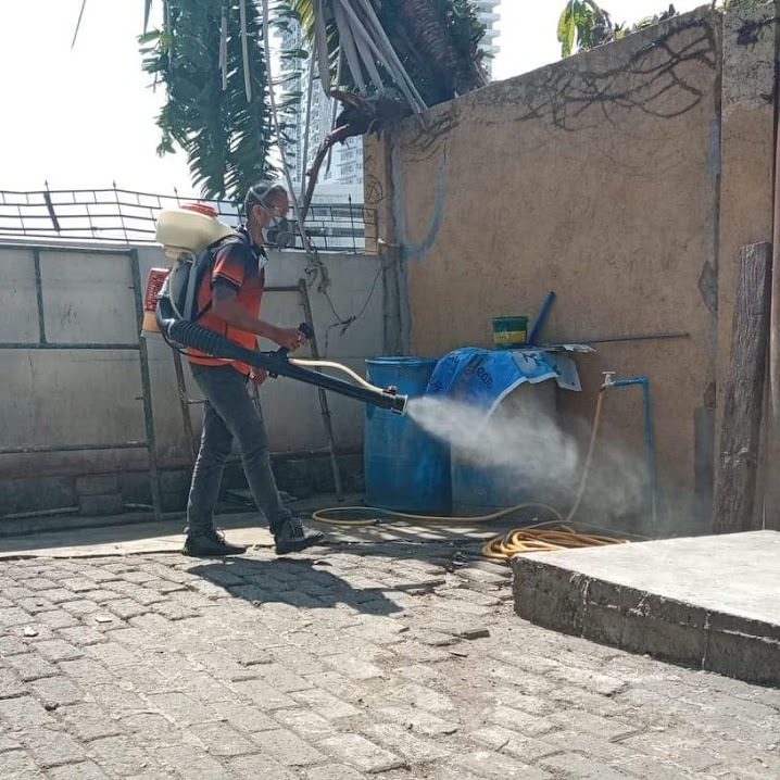 A pest control worker using a motorized mist blower for outdoor fogging and disinfectant spraying.
