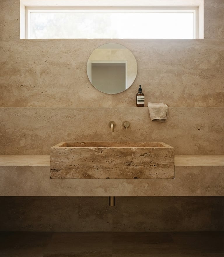 Straight-on architectural composition of a monolithic travertine bathroom basin, soft morning light filtering through a high window, neutral earth tones, medium format film.