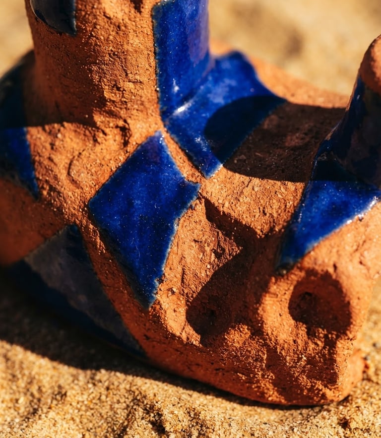 Extreme close-up of a vibrant terracotta and cobalt blue sculptural ceramic object on a warm sand background, hard direct sunlight casting dramatic sharp shadows, macro texture, 35mm lens