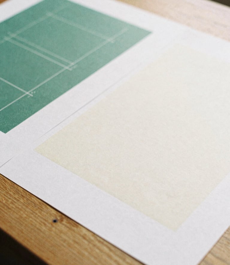 Close-up of physical design proofs on a heavy oak table, soft overcast British daylight, muted forest green and warm cream tones, 35mm film grain