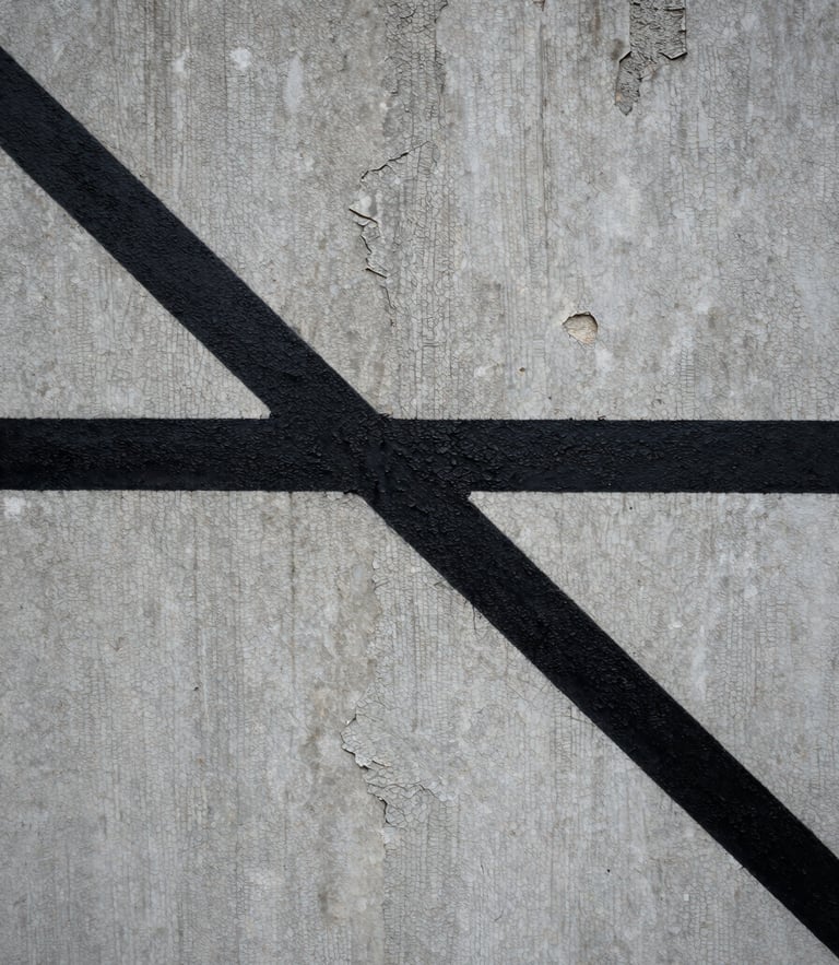 Extreme close-up of a sharp, stark black painted line cutting across a crumbling, textured grey concrete wall under overcast daylight.