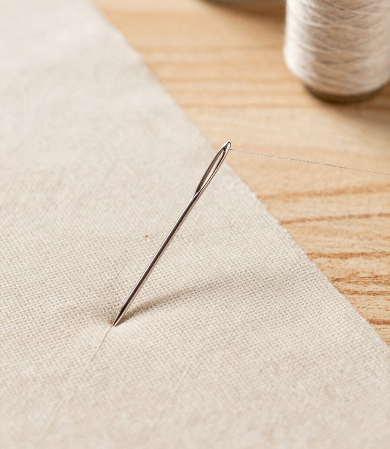 Macro detail of a silver sewing needle threading fine beige linen fabric on a clean, sunlit wooden workspace, high-end atelier style, 50mm.