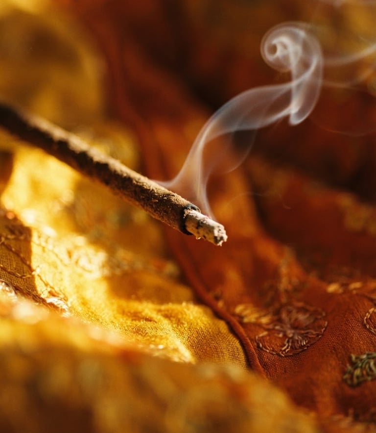 luxurious editorial photography of a single hand-rolled incense stick, delicate curl of pale grey smoke rising in dramatic golden-hour side light, rich saffron background, macro depth of field, 35mm