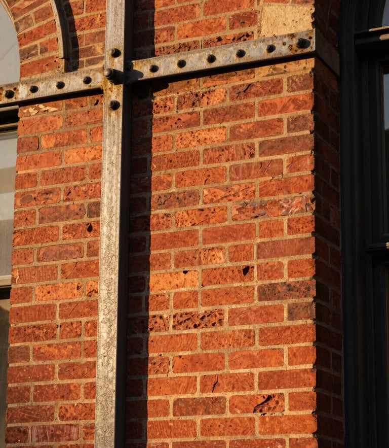 Close-up of historic St. Louis red brick masonry and weathered iron framing under warm golden hour light, showing solid architectural textures.
