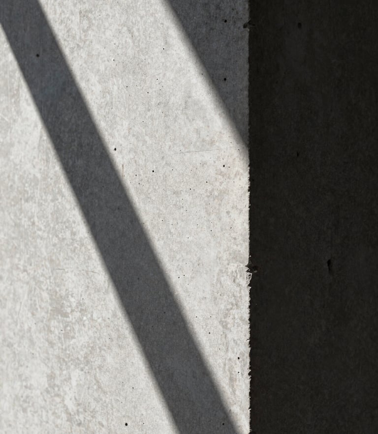 Extreme close-up of board-formed concrete texture under harsh midday sun, casting deep, sharp-edged architectural shadows.