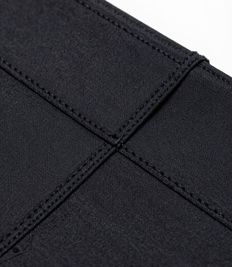 Macro detail shot of a black technical compression fabric weave, showing double-stitched seams and precise texture, bright cool-toned studio light, sharp focus