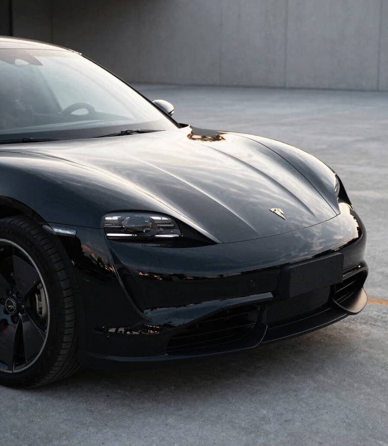 Close-up of a luxury electric car parked in a modern, minimalist concrete driveway in Budapest, soft morning light reflecting off the pristine, freshly detailed black paintwork.