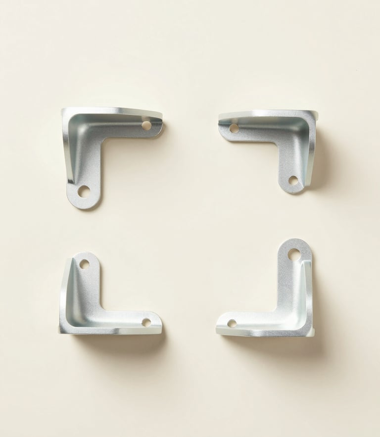 Overhead minimalist flat-lay of custom machined aluminum brackets on a soft pastel cream background, clean studio lighting, 50mm