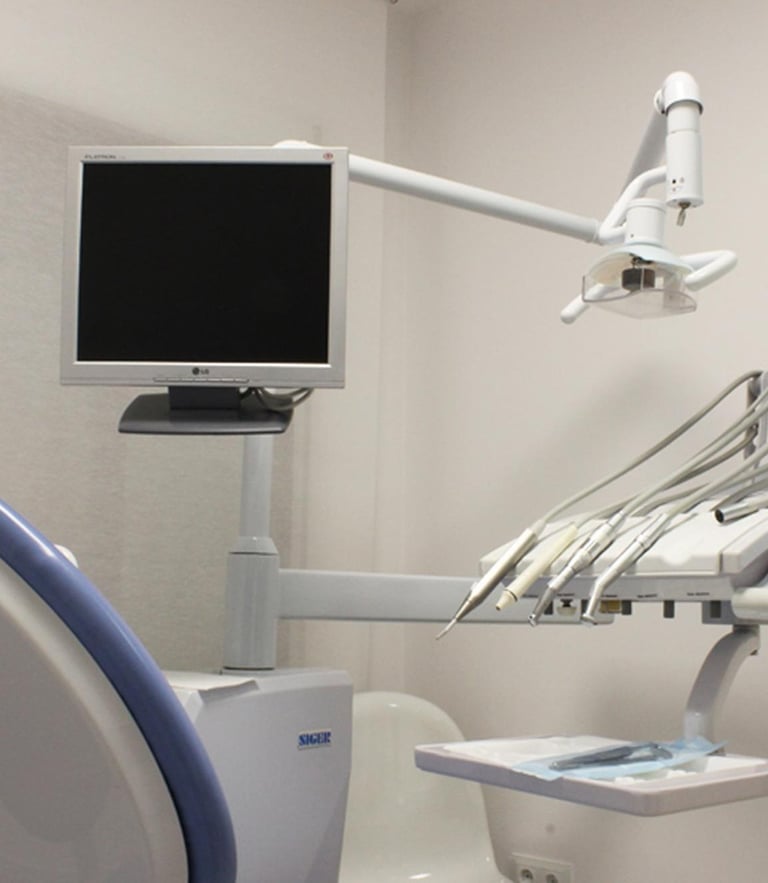 Modern dental examination room featuring an ergonomic chair, overhead monitor, and medical tool console.