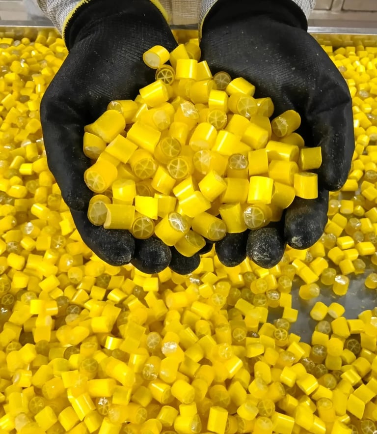 Gloved hands holding a pile of yellow lemon hard candies with a citrus cross-section design.