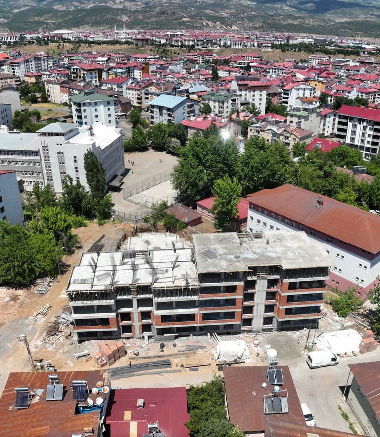Aerial view of an apartment building under construction in a Turkish city with red-roofed houses.