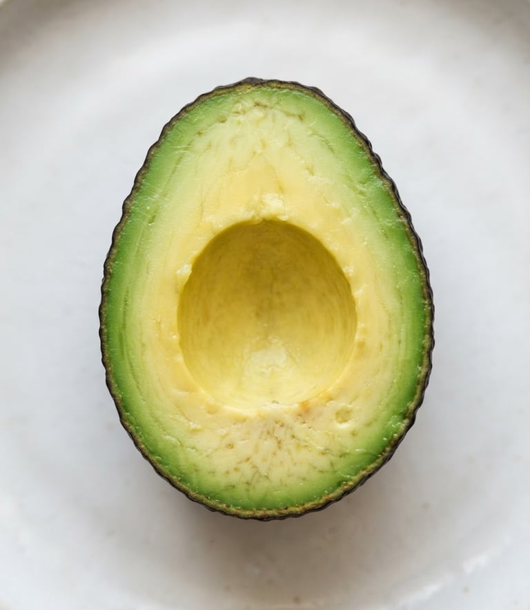 Top-down macro shot of sliced avocado showing rich green-to-yellow gradient flesh on a clean off-white surface, soft morning light