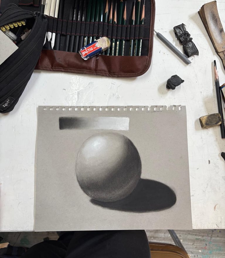Shaded pencil drawing of a sphere on gray paper with art supplies and drawing pencils.