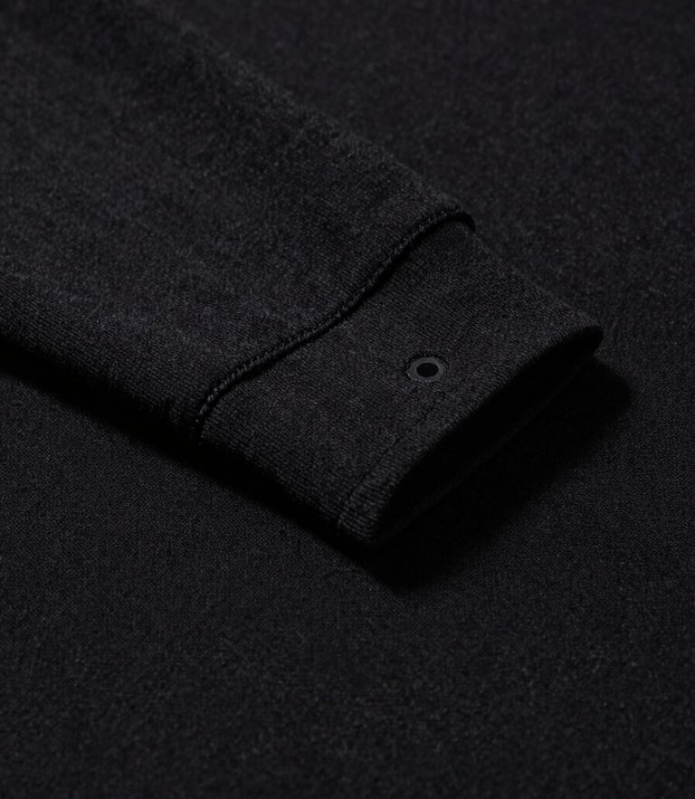 Low-angle close-up of premium heavyweight black cotton fabric texture, showing double-needle stitching on the collar, sharp high-contrast studio lighting with deep shadows.