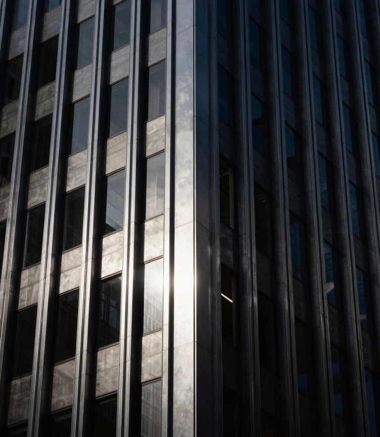 Moody architectural detail of a modern financial skyscraper facade, low-key dramatic lighting with sharp silver reflections, deep charcoal metallic textures, high contrast, 35mm