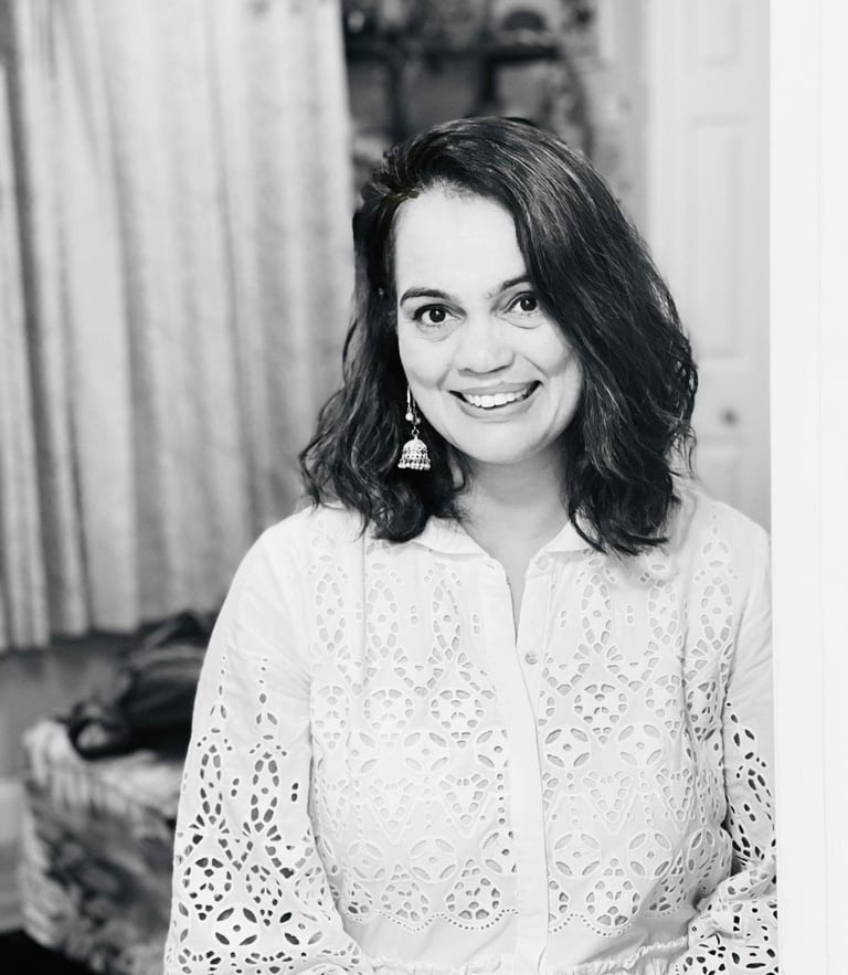 Smiling woman with wavy hair wearing a white eyelet lace blouse and jhumka earrings.