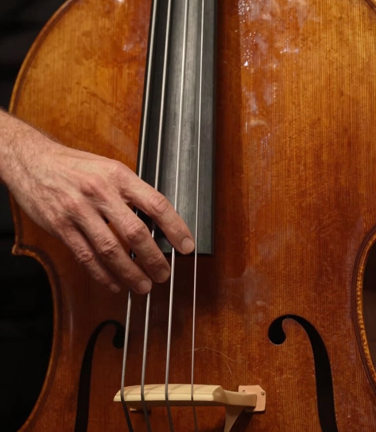 Tactile close-up of hands navigating the fingerboard of an antique upright bass, warm low-key amber lighting highlighting the wood grain