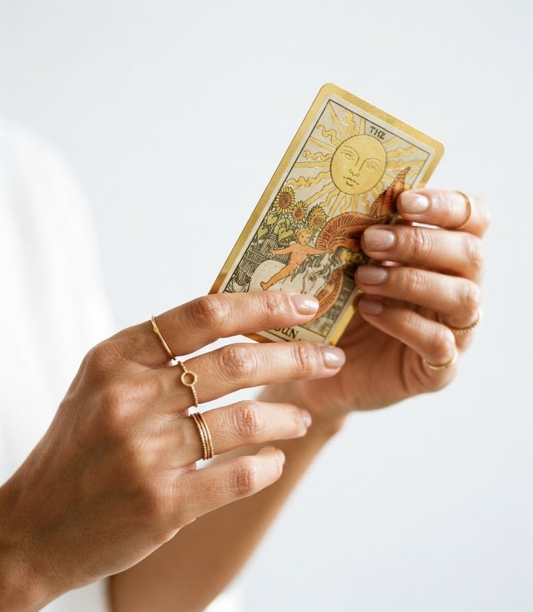 Close-up macro shot of hands with delicate gold rings holding a gold-rimmed tarot card, bright natural daylight, soft golden highlights, minimalist white background, 35mm