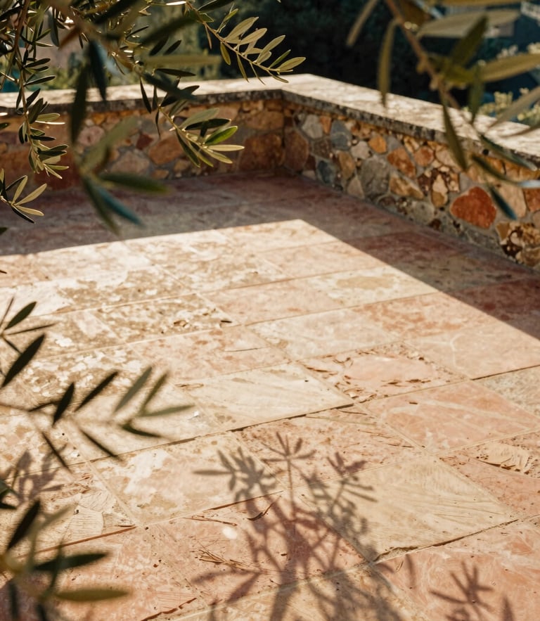 A quiet sun-dappled stone terrace with olive branches casting soft shadows on a terracotta floor, warm golden hour light, 35mm film aesthetic.