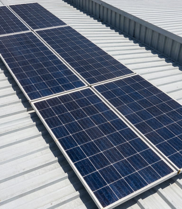 High-angle shot of clean solar panels installed on a modern industrial metal roof in Colombia, bright direct midday sunlight, sharp geometric shadows, high-contrast technical framing.
