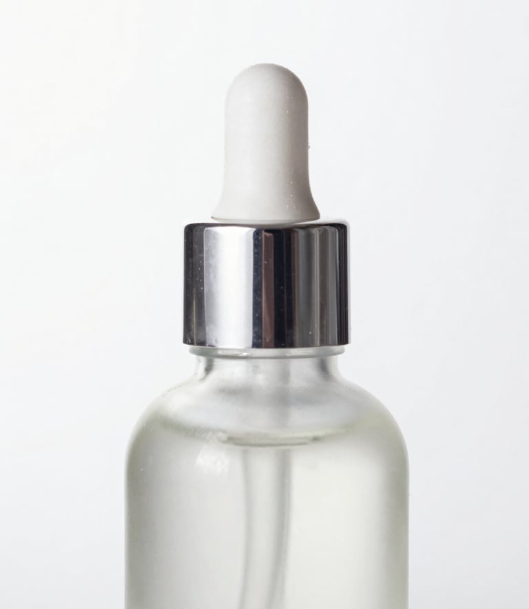 High-key product photography of a single airless glass bottle reflecting crisp studio light with soft silver reflections, clean white background, macro lens, sharp focus