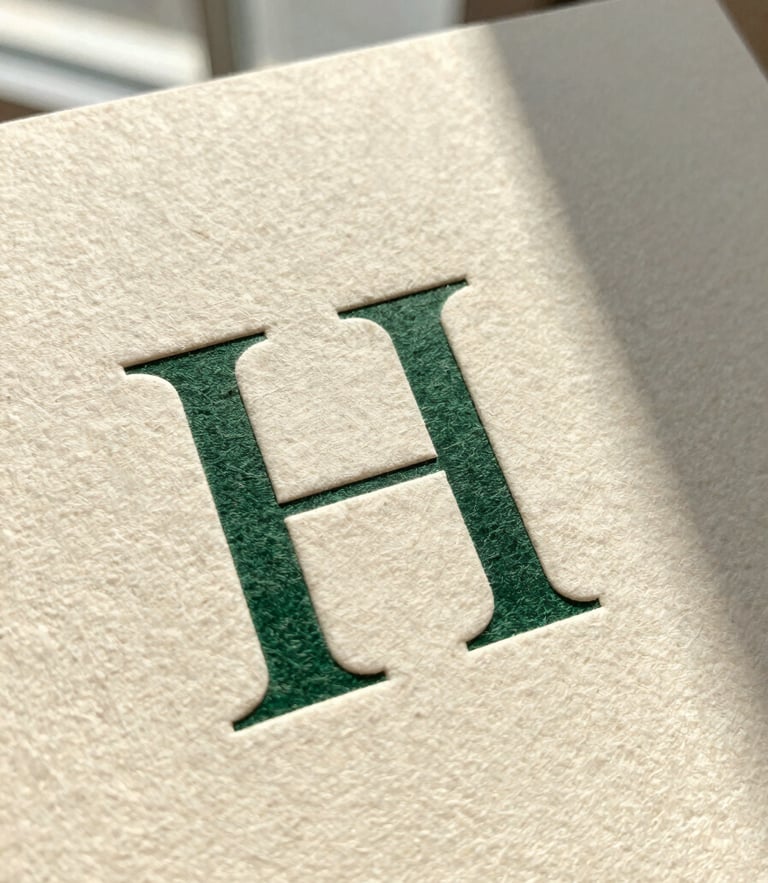 Macro shot of a heavy-weight textured cotton paper card with crisp debossed serif typography, natural side-lit window daylight casting soft shadows, warm cream tone.