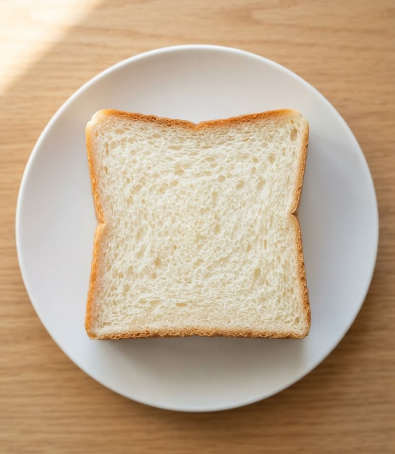 Dead-on geometric overhead shot of a perfectly square shokupan slice on a minimalist white plate, bright morning window light highlighting the uniform crumb structure, warm golden crust edges.