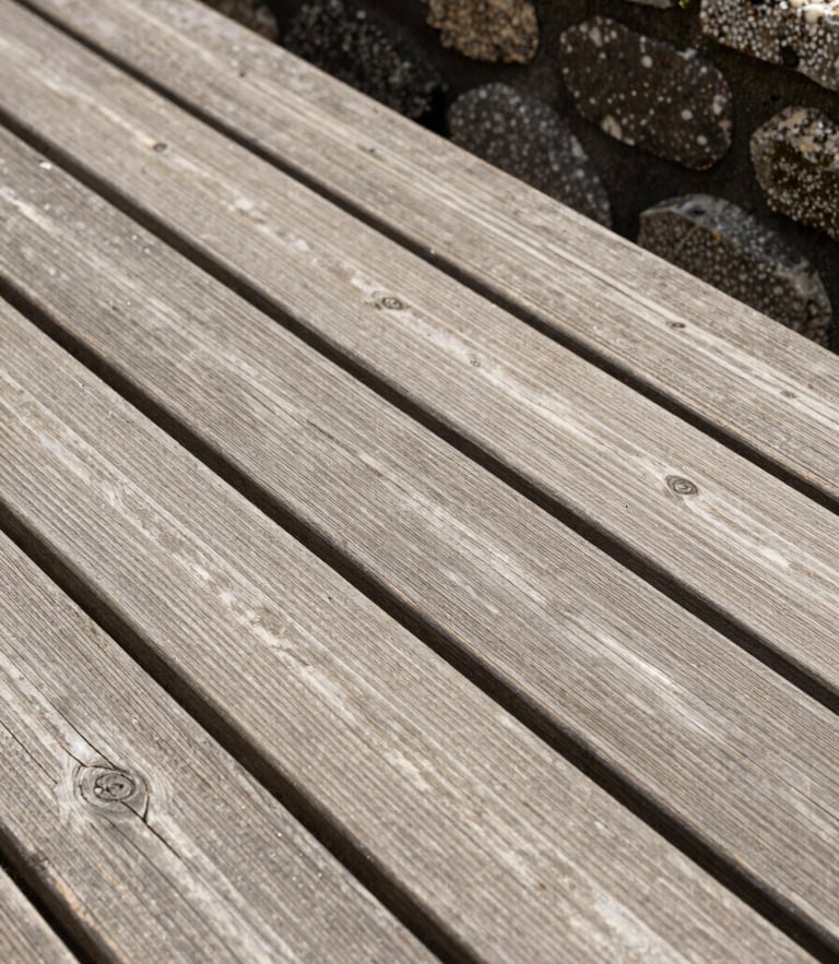 Vue rapprochée d'une terrasse en bois de qualité supérieure, les lames de bois s'ajustent parfaitement contre un muret en pierre de taille, lumière naturelle vive.
