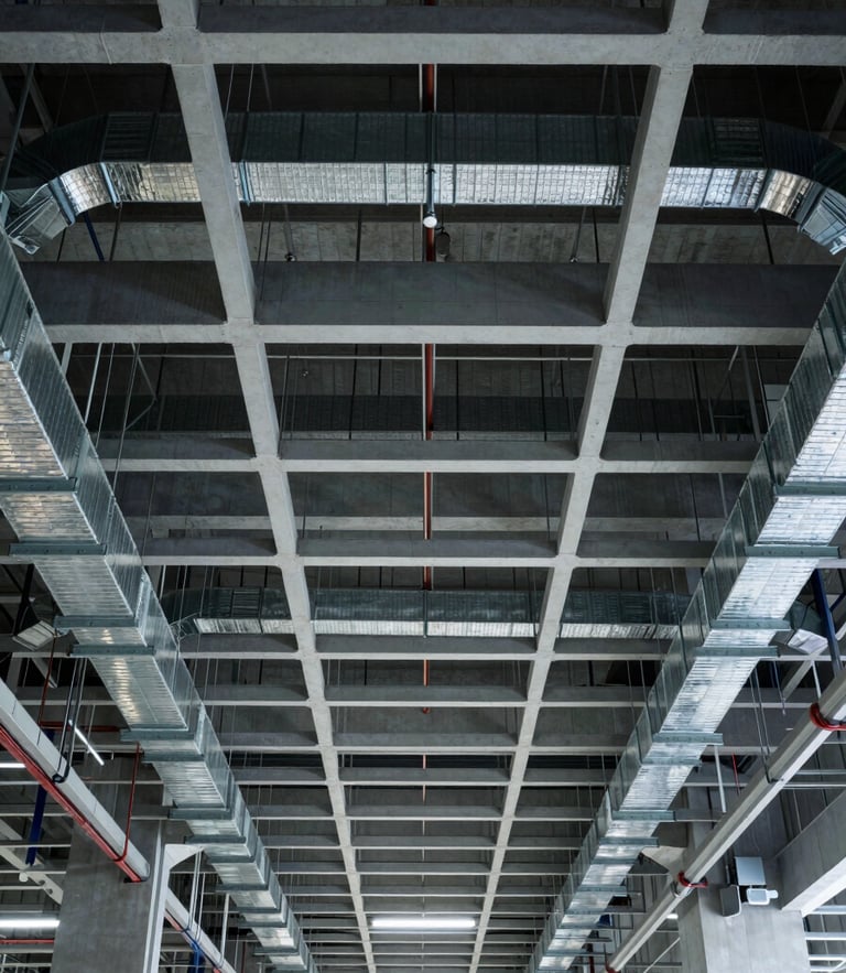 High-contrast orthographic view looking directly up at a perfectly aligned ceiling grid of exposed ductwork, cable trays, and color-coded piping in a modern industrial facility, sharp shadows, cool ambient light.