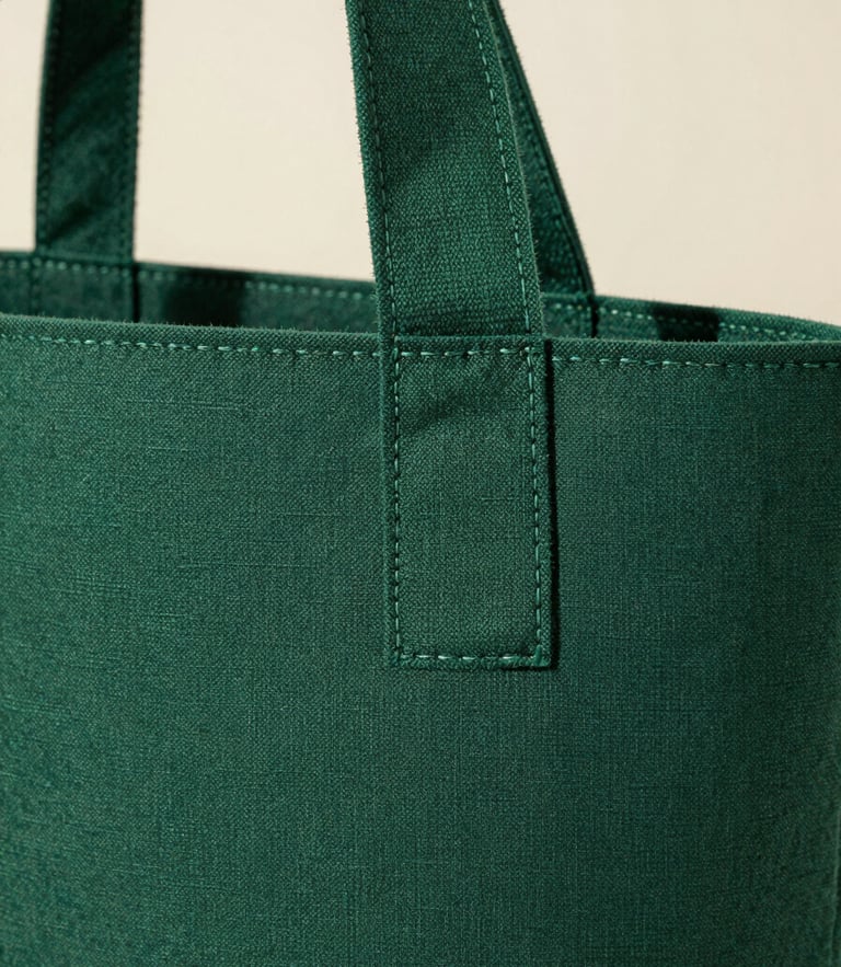 Macro detail of a deep forest green nonwoven bag handle, showing clean ultrasonic weld seams and raw spunbond fabric texture under bright daylight