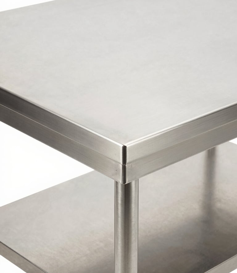 Crisp industrial product photography, bright high-key studio lighting, close-up of a premium commercial stainless steel prep table with perfect seamless joints, clean metallic reflections, sharp focus