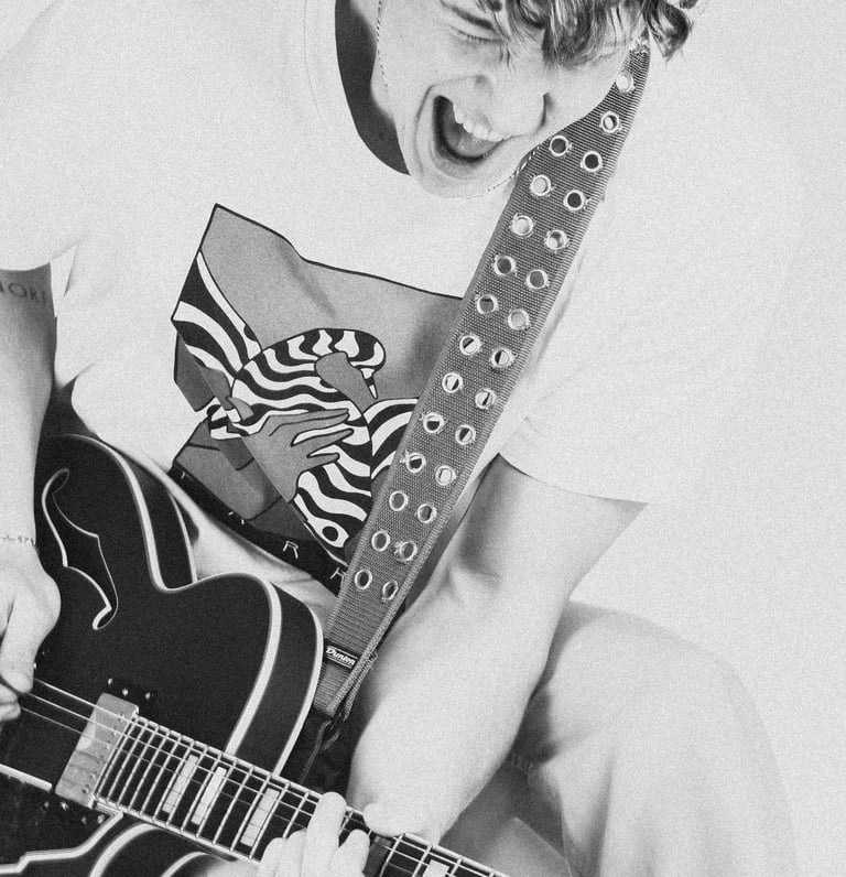 portrait of a man jumping in a white shirt and tie dye on a guitar