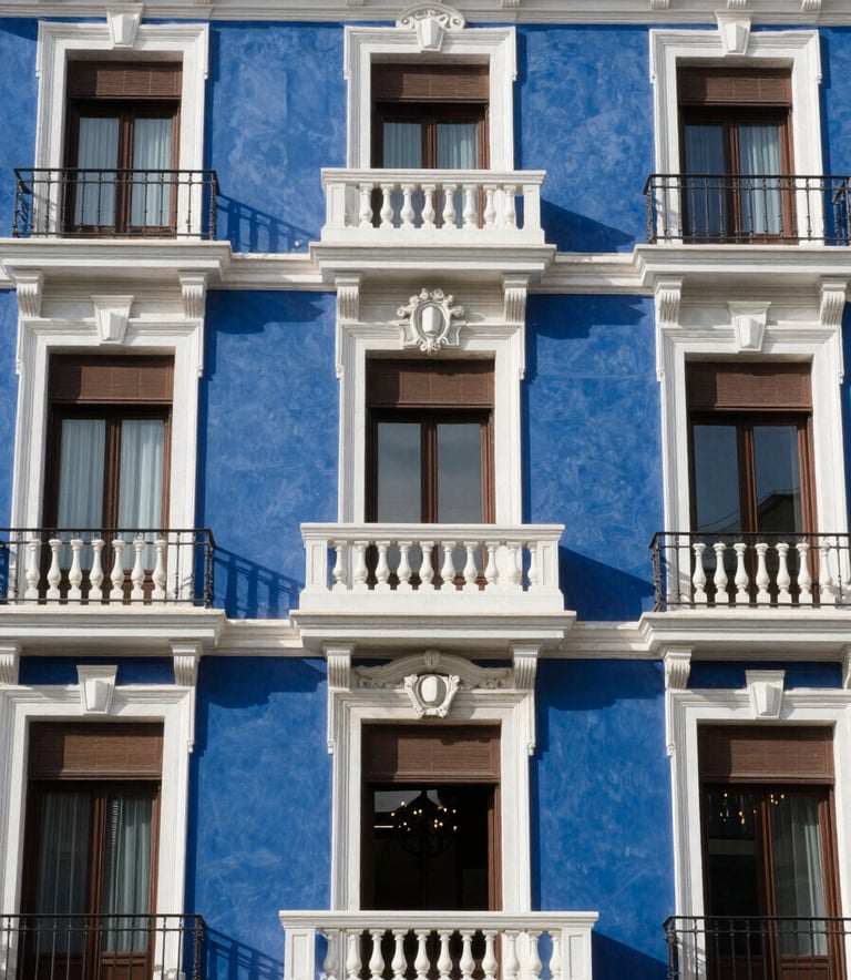 Architectural detail of a classic, high-end residential building facade in Madrid, Spain. The lighting is bright and clear, emphasizing the integrity and history of the location, with colors reflecting deep blue and white.