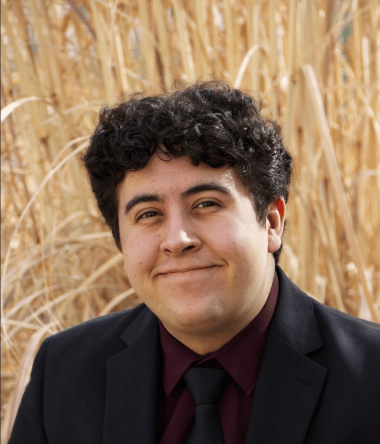 Image of Gregg in a black suit behind is tall grass.