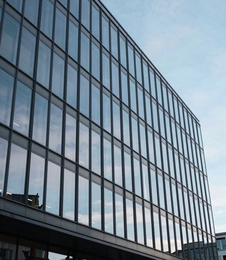 A wide-angle photography shot of a modern, clean glass building facade in Cardiff, Wales, reflecting a soft blue sky. The composition is professional and authoritative, using a palette of slate blue and light grey to suggest stability.